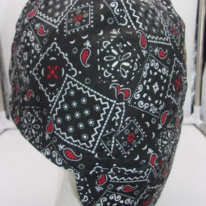 May include: Black and white bandana pattern welding cap with red accents. The cap is made of a durable fabric and is designed to protect the wearer's head and neck from sparks and heat.