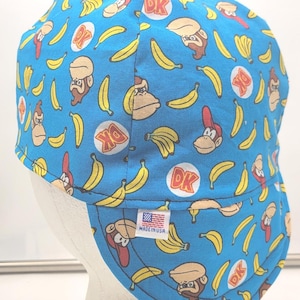 May include: A blue welding cap with a pattern of yellow bananas and Donkey Kong characters. The cap has a red, white, and blue "Made in USA" label.