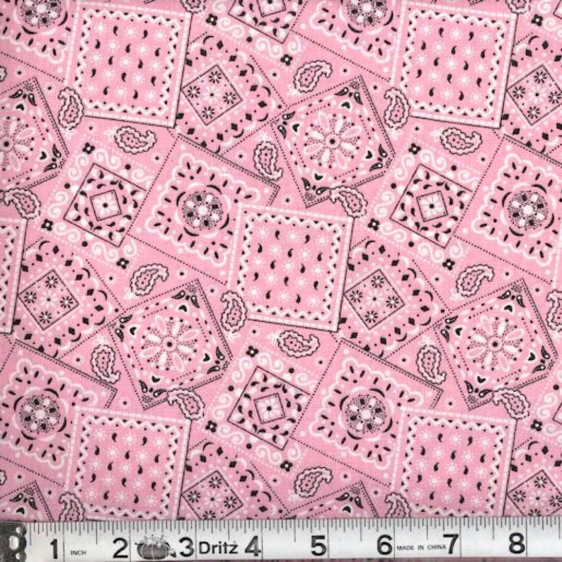 May include: Pink fabric with a repeating pattern of black and white bandana designs. The fabric is measured with a ruler in inches.