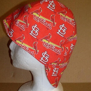 May include: Red baseball cap with a St. Louis Cardinals pattern. The cap has a flap that covers the ears and neck.