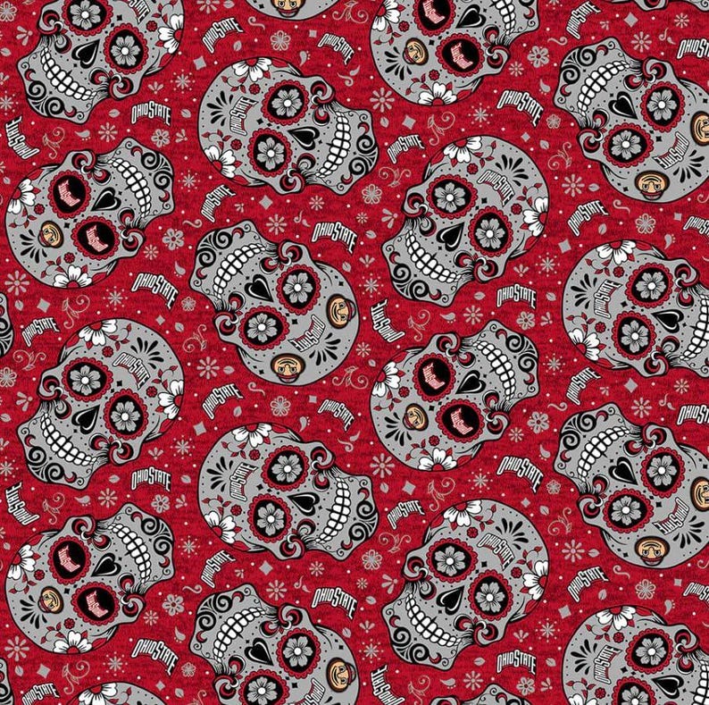 May include: A red fabric featuring a repeating pattern of grey sugar skulls decorated with white flowers, black swirls, and the text Ohio State. The skulls are oriented in various directions across the vibrant red background.