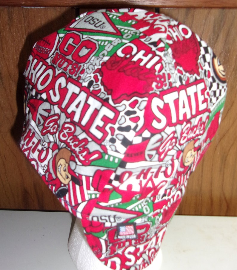 May include: A fabric cap featuring a repeating pattern of Ohio State University graphics in red, white, and green. The design includes the text OHIO STATE, Go Bucks, and OSU pennants. A small rectangular tag on the side reads MADE IN USA.