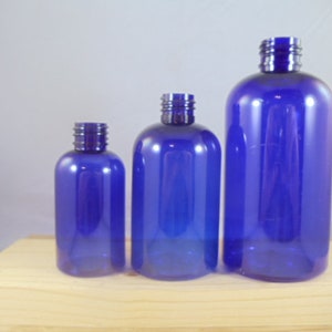 Puede incluir: Tres botellas de pl&aacute;stico azules de diferentes tama&ntilde;os. Las botellas son transparentes y tienen un ligero tono azul. Todas est&aacute;n de pie sobre una superficie de madera.