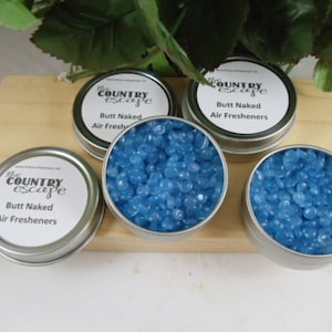 May include: Four small, silver, round tins filled with blue wax beads. Each tin has a white label with the text "The Country Escape" and "Butt Naked Air Fresheners".