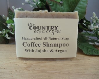 May include: A bar of handcrafted all-natural coffee shampoo soap with jojoba and argan oil. The soap is labeled "the country escape" and "Coffee Shampoo with Jojoba & Argan".