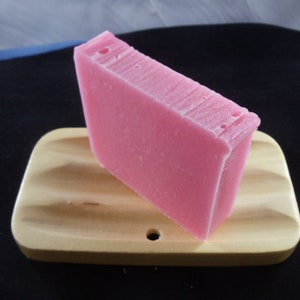 May include: A pink bar of soap on a wooden soap dish. The soap dish has a wavy design.