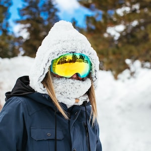 Puede incluir: Una persona con una chaqueta de invierno azul con capucha forrada de piel blanca y gafas de esqu&iacute;. Las gafas tienen una lente reflectante que muestra un paisaje nevado.