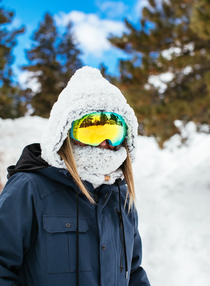 Puede incluir: Una persona con una chaqueta de invierno azul con capucha forrada de piel blanca y gafas de esqu&iacute;. Las gafas tienen una lente reflectante que muestra un paisaje nevado.