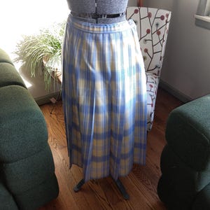 May include: A vintage, pleated skirt in a blue and yellow plaid pattern. The skirt is displayed on a dress form. The fabric has a soft, flowing drape. The skirt is a classic style, suitable for various occasions.