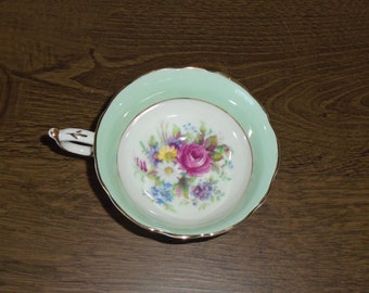 May include: A vintage teacup with a floral design. The cup is white with a green rim and gold trim. The floral design features a pink rose and other flowers in shades of pink, purple, blue, and yellow.