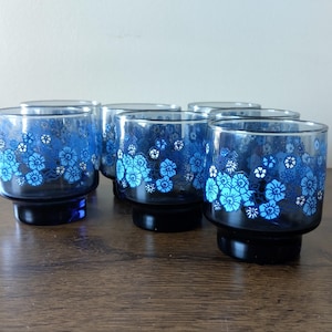 May include: Set of six vintage blue drinking glasses with a floral design. The glasses have a dark blue base and are decorated with light blue and white flowers. The glasses are made of glass and are suitable for serving beverages.