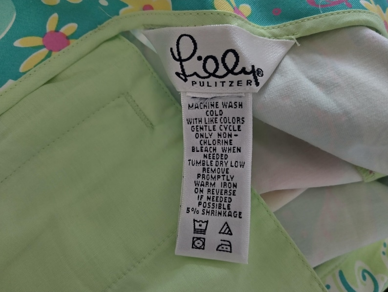 May include: A light green garment featuring a white fabric care label with the text Lilly Pulitzer. The label includes washing instructions: machine wash cold, gentle cycle, non-chlorine bleach, tumble dry low, and warm iron on reverse if needed.