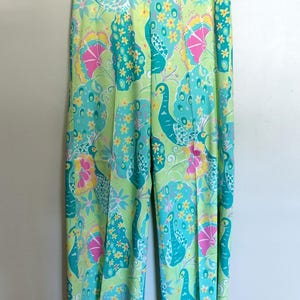 May include: Wide-leg trousers featuring a vibrant, multi-coloured peacock and floral pattern. The design includes shades of lime green, turquoise, hot pink, and yellow. These trousers have a straight-cut silhouette and are displayed on a clear hanger.