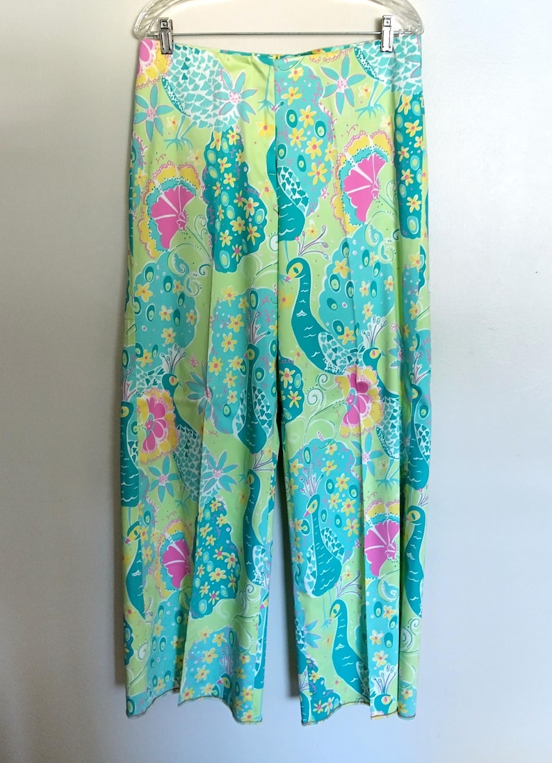 May include: Wide-leg trousers featuring a vibrant, multi-coloured peacock and floral pattern. The design includes shades of lime green, turquoise, hot pink, and yellow. These trousers have a straight-cut silhouette and are displayed on a clear hanger.