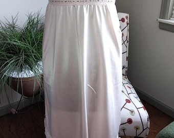 May include: A white slip skirt with lace trim at the waist and hem. The skirt is made of a silky material and is a vintage style.