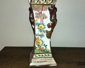 May include: A white porcelain vase with a floral design and brown wooden handles. The vase has a square base and a rectangular body.