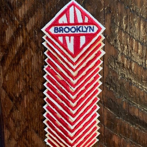 May include: A stack of 12 red and white diamond-shaped patches with the word "BROOKLYN" embroidered in blue on the top patch.