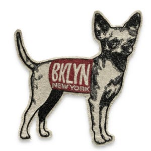 May include: Embroidered patch in the shape of a Chihuahua dog. The dog is black and white with a red rectangle on its side that reads "BKLYN NEW YORK" in white letters. The patch has a cream-colored background.