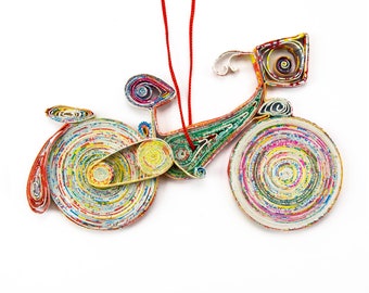 May include: A colorful paper bicycle ornament with red string for hanging. The bicycle is made of rolled up paper with a variety of colors and patterns.