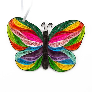 May include: A butterfly-shaped paper quilling ornament featuring a black body and antennae. The wings are composed of tightly coiled paper strips in vibrant shades of yellow, orange, red, pink, purple, blue, and green, with a white ribbon loop.