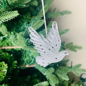 May include: White paper dove Christmas ornament with a string for hanging. The dove is decorated with small, clear rhinestones.