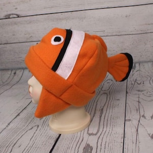 May include: Orange and white fleece hat shaped like a clownfish with black stripes and a black eye.