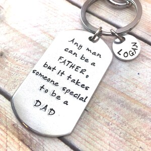 May include: Silver keychain with a dog tag charm that reads "Any man can be a father, but it takes someone special to be a dad."  A smaller silver charm with the name "Logan" is attached to the keychain.