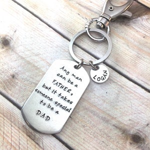 May include: Silver keychain with a silver tag that reads "Any man can be a FATHER. But it takes someone special to be a DAD." and a smaller silver tag that reads "LOGAN".