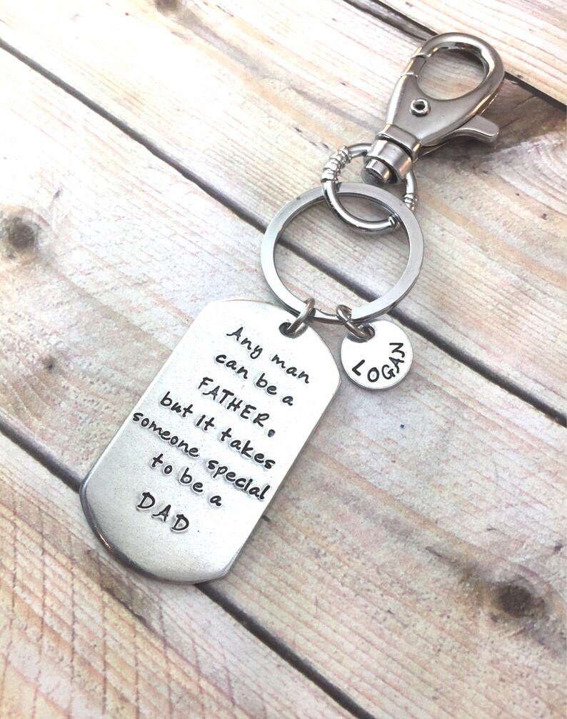 May include: Silver keychain with a silver tag that reads "Any man can be a FATHER. But it takes someone special to be a DAD." and a smaller silver tag that reads "LOGAN".