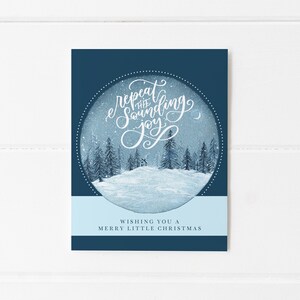 May include: A blue Christmas card with a white circle in the center. The circle contains a snowy winter scene with a small house and trees. The text "repeat the sounding joy" is written in white cursive inside the circle. The text "Wishing you a Merry Little Christmas" is written in white at the bottom of the card.