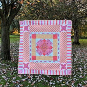 May include: A pink and orange patchwork quilt with a star design in the corners. The quilt is made of different fabrics with geometric patterns.