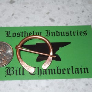 May include: A copper ring brooch with a pin, on a green card with the text "Losthelm Industries Bill Chamberlain".