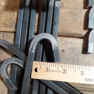 May include: Close-up of a stack of black metal hooks with rounded ends. A wooden ruler with the text "MADE IN U.S.A." is visible in the image.