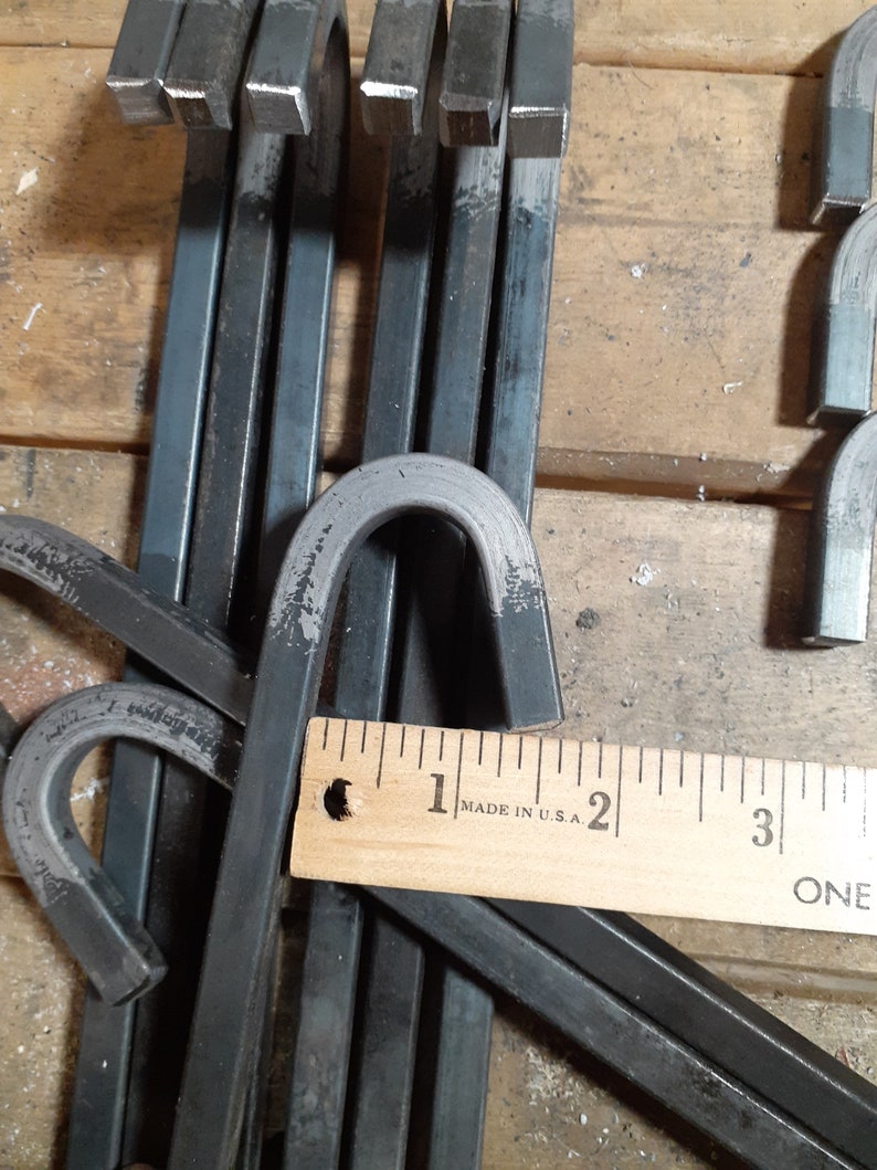 May include: Close-up of a stack of black metal hooks with rounded ends. A wooden ruler with the text "MADE IN U.S.A." is visible in the image.