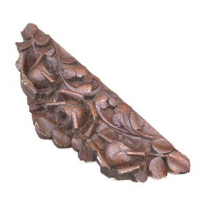 May include: A carved wooden decorative element with a dark brown finish. The piece features intricate floral and leaf designs, with visible details of carved roses and foliage. The edges show slight wear and a touch of gold paint.