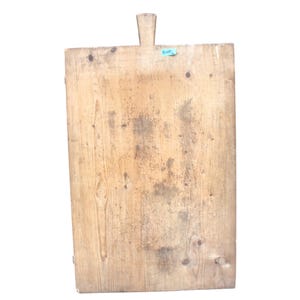 May include: A rectangular light brown wooden cutting board with a prominent vertical wood grain pattern, natural knots, and a small handle at the top center. A small blue rectangular sticker with the handwritten text 8099 is attached to the surface.