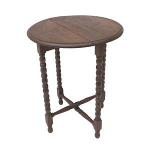 May include: A round, dark brown wooden side table featuring a smooth, circular tabletop surface and four slender, turned legs. The legs are connected by a central X-shaped cross-stretcher support structure, providing stability to the furniture piece.