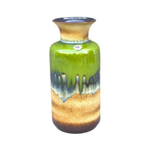 May include: A ceramic vase with a flared top and a rounded body. The vase has a glossy finish with a colour gradient, transitioning from a dark brown base to tan, green, and a dark blue-grey rim. A small, circular sticker is visible.