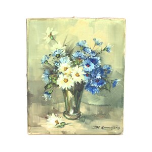 Puede incluir: Pintura al óleo de un arreglo floral en un jarrón plateado. El ramo presenta flores blancas y azules con tallos y hojas verdes. El fondo es verde y gris apagado. La pintura está firmada en la esquina inferior derecha.