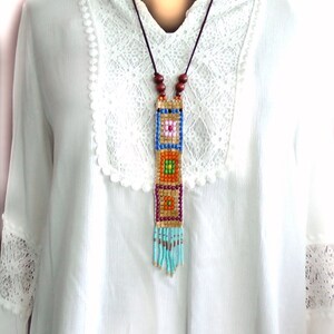May include: A long beaded necklace with a colorful geometric pattern and a turquoise fringe. The necklace is made of small, colorful beads and is strung on a brown cord.