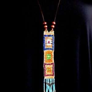May include: A colorful beaded necklace with a geometric pattern and a tassel. The necklace is made of small, square beads in shades of blue, green, orange, and brown. The tassel is made of turquoise beads.