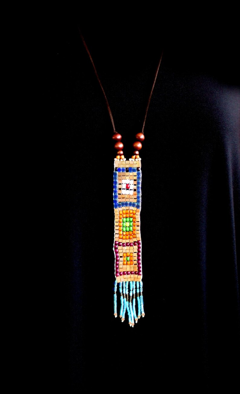 May include: A colorful beaded necklace with a geometric pattern and a tassel. The necklace is made of small, square beads in shades of blue, green, orange, and brown. The tassel is made of turquoise beads.