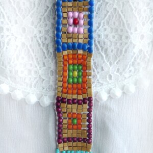 May include: A colorful beaded necklace with a geometric pattern and a turquoise tassel. The necklace is made of wooden beads and features a variety of colors, including blue, orange, green, and pink.