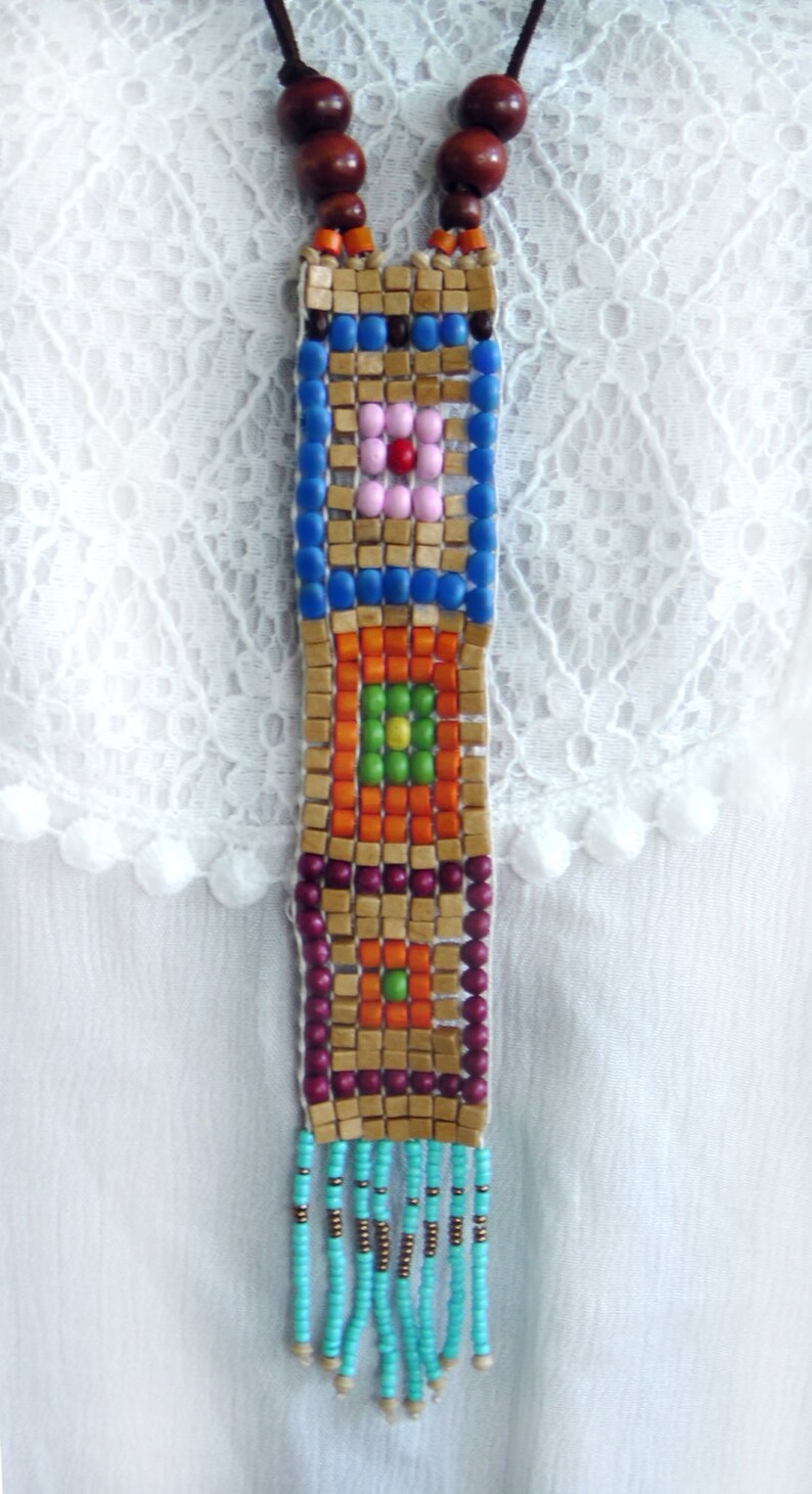 May include: A colorful beaded necklace with a geometric pattern and a turquoise tassel. The necklace is made of wooden beads and features a variety of colors, including blue, orange, green, and pink.