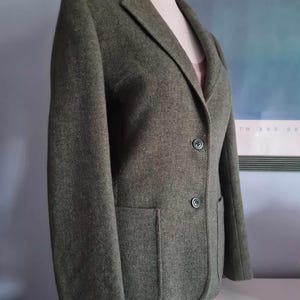 May include: A dark green blazer with a single button closure and a patch pocket on the left side.