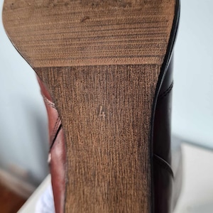 May include: Close-up of the bottom of a brown leather boot with a wooden heel. The heel has a size 4 printed on it.