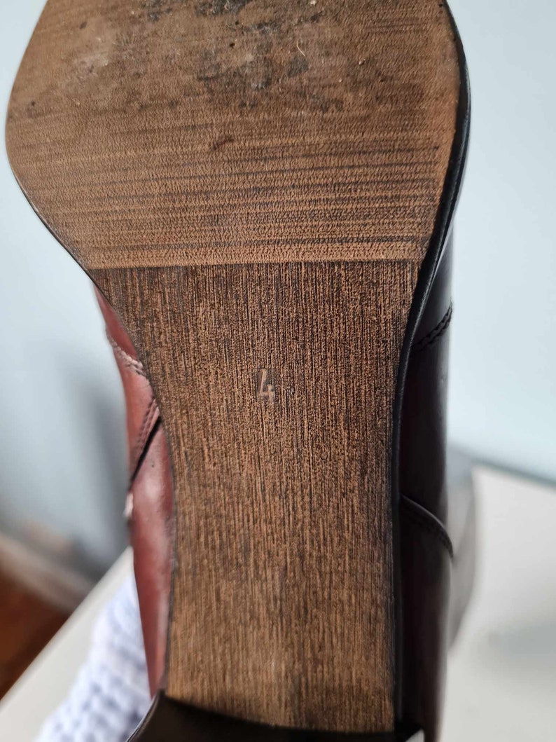 May include: Close-up of the bottom of a brown leather boot with a wooden heel. The heel has a size 4 printed on it.