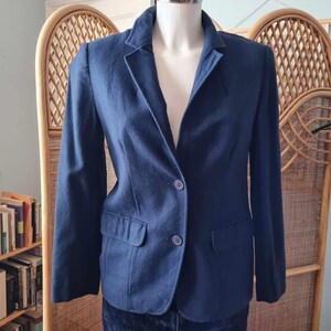 May include: A dark blue blazer with a single-breasted closure and two button pockets. The blazer is on a mannequin and has a classic, tailored fit.