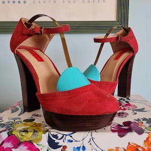 Peut inclure: Une paire de talons hauts plateforme en daim rouge avec des brides à la cheville et une fermeture à boucle. Les talons mesurent environ 10 cm de haut et ont une plateforme en bois.
