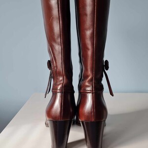 May include: A pair of brown leather knee-high boots with a block heel and a decorative tie at the back of the ankle.
